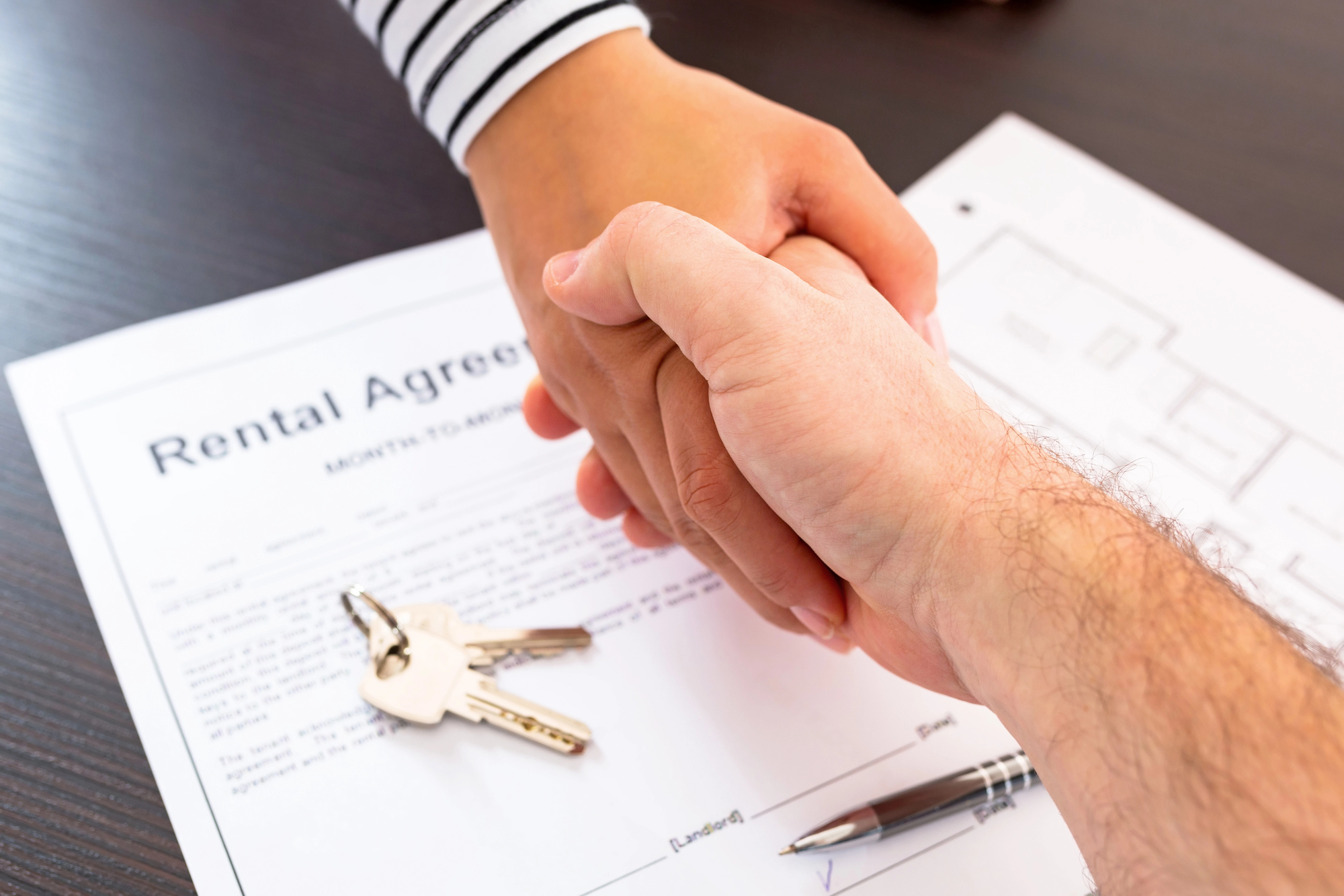 Two people shaking hands on top of a rental agreement