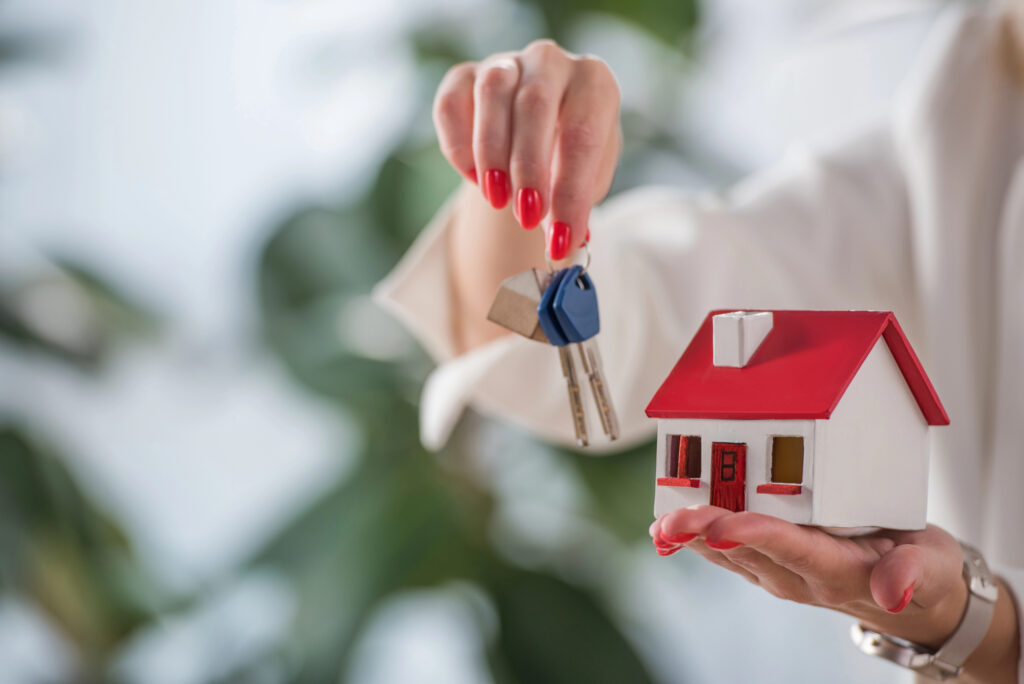 Woman holding house keys in one hand and a dummy house in another hand