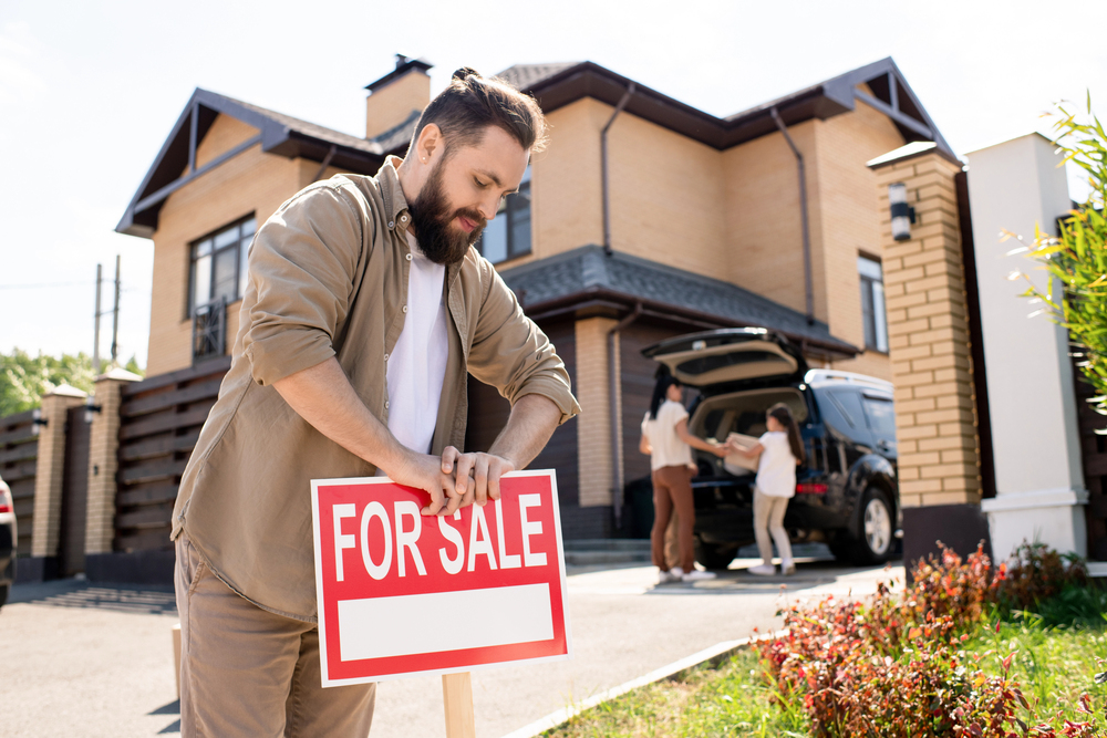 a man installing a for sale sign in front of his mansion